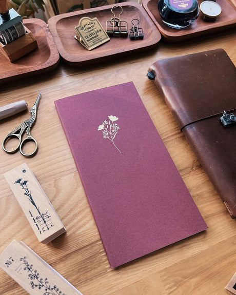 Purple notebook with floral design on a wooden surface with stationery items.
